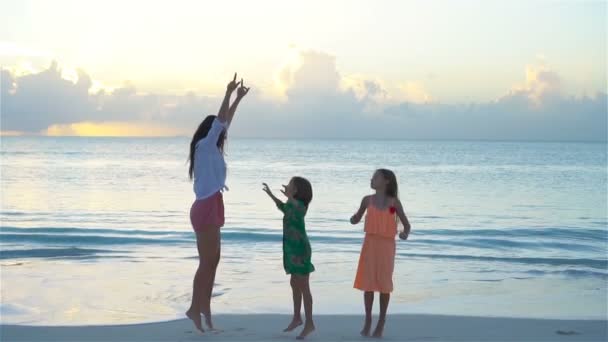 Kleine schattige meisjes en jonge moeder op tropisch strand in warme avond dansen en plezier. Familie bij zonsondergang — Stockvideo