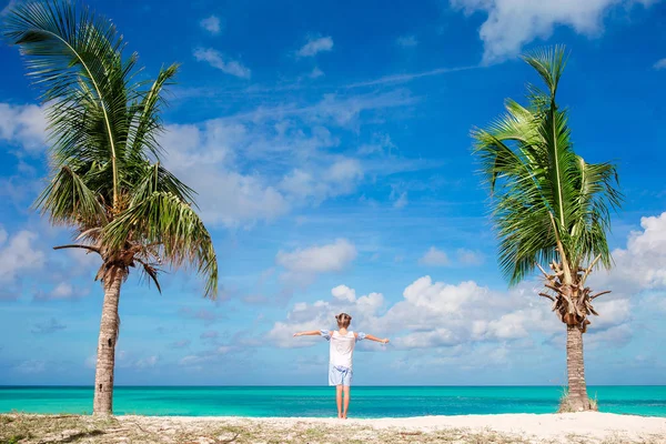 Симпатичная девчонка в белом платье на пляже во время карикатурных каникул. Очаровательный ребенок стоит между пальмами на острове Антигуа — стоковое фото