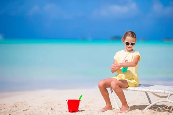 Little adorable girl with bottle of sun cream sitting at tropical beach — Stock Photo, Image