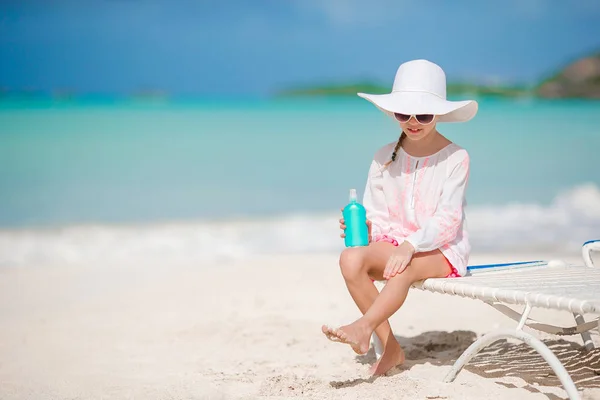 Petite adorable fille avec bouteille de crème solaire assise à la plage tropicale — Photo