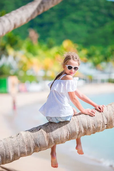 Little girl on palm tree at tropical seashore — Stock Photo, Image