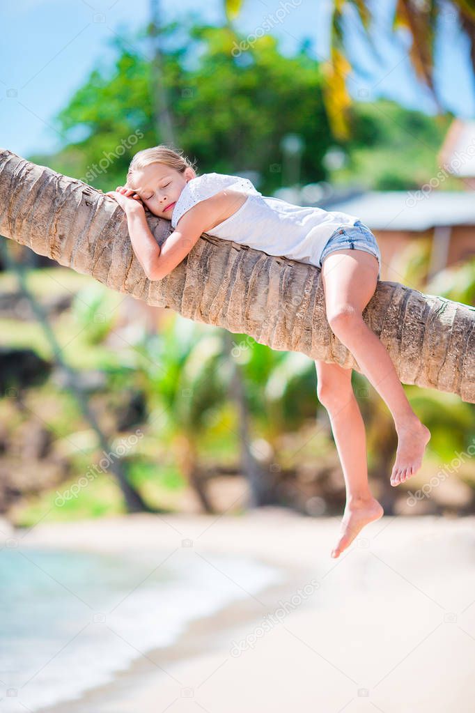 Little girl at tropical beach on palm tree during summer vacation
