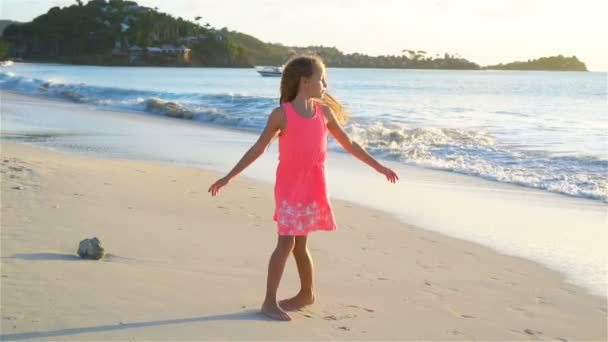 Αξιολάτρευτο ευτυχισμένη μικρό κορίτσι έχει τη διασκέδαση στην παραλία με λευκή κατά το ηλιοβασίλεμα. Βίντεο αργής κίνησης — Αρχείο Βίντεο