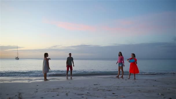 Família feliz brincando com disco voador na praia ao pôr do sol — Vídeo de Stock