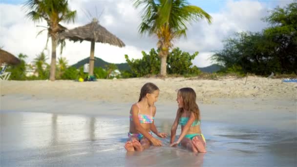 Holčičky, hraní s pískem na pláži. Děti sedí v mělké vodě a dělat hrad z písku — Stock video