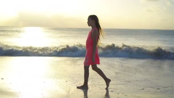 Изображение маленькой девочки, прогуливающейся по пляжу на закате . — стоковое видео
