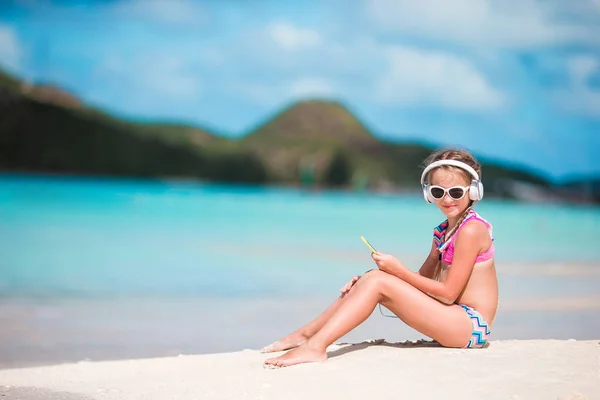 Kleines entzückendes Mädchen am Strand, das die Musik mit großen Kopfhörern hört — Stockfoto