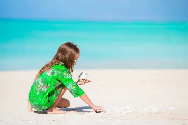 Niña linda con concha en las manos en la playa tropical. Adorable niña jugando con conchas marinas en la playa — Foto de Stock