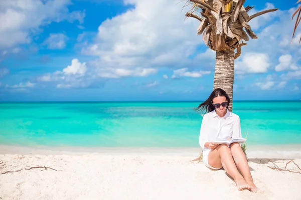 Ung kvinna läsa på tropiska stranden nära palm tree — Stockfoto