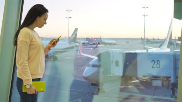 항공 여객 비행 항공기에 대 한 대기 하는 공항 라운지에서. 백인 여자 큰 창 배경 근처 핸드폰으로 큰 비행기 이야기 — 비디오