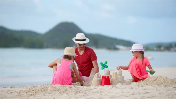 Отец и две девочки играют с песком и строят замок из песка на тропическом пляже — стоковое видео
