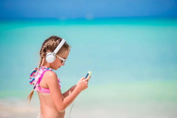 Niña adorable escuchando música por teléfono celular en la playa — Foto de Stock