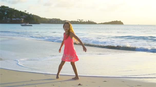 Αξιολάτρευτο ευτυχισμένη μικρό κορίτσι έχει τη διασκέδαση στην παραλία με λευκή κατά το ηλιοβασίλεμα. Βίντεο αργής κίνησης — Αρχείο Βίντεο