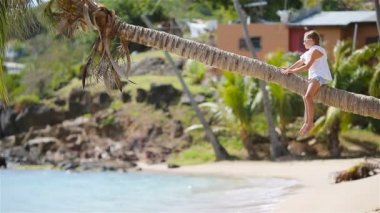 Yaz tatili boyunca tropik sahilde palmiye ağacında oturan sevimli küçük kız.