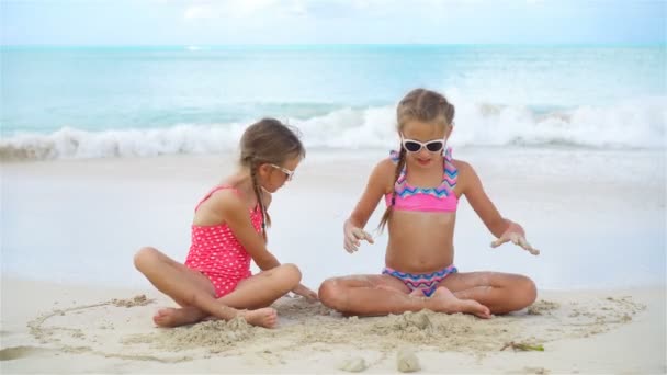 愛らしい女の子がビーチで楽しみがたくさんをあります。海岸で砂で遊んで 2 人の美しい子供 — ストック動画