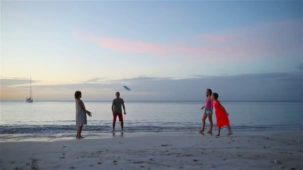 Família feliz brincando com disco voador na praia ao pôr do sol — Vídeo de Stock