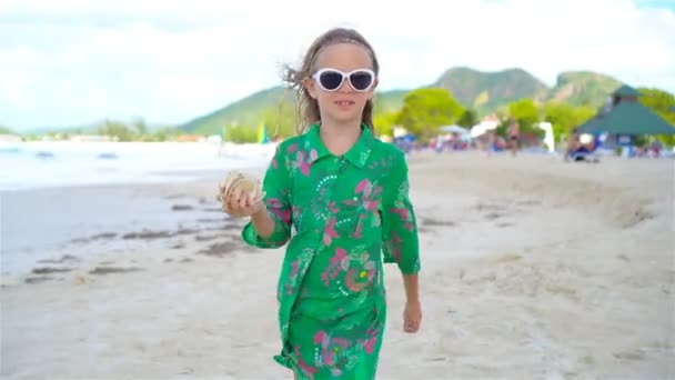Kleines süßes Mädchen mit Muschel in den Händen am tropischen Strand. entzückendes kleines Mädchen spielt mit Muscheln am Strand — Stockvideo