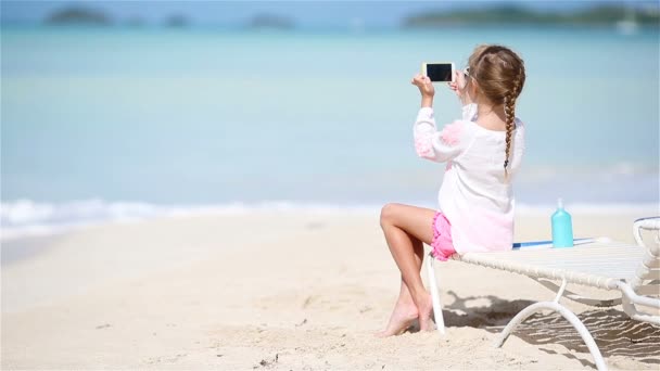 Liten flicka vilket gör video eller foto med hennes kamera som sitter på chaise-loungen — Stockvideo