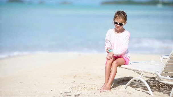 Маленькая девочка с бутылкой крема для загара на тропическом пляже — стоковое видео
