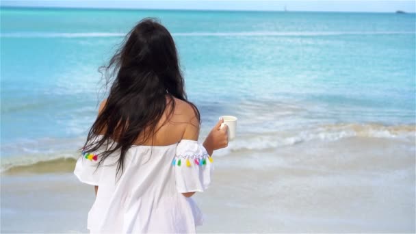 Mujer joven con taza de bebida caliente en la playa tropical blanca. Lento movimiento. Vista trasera de la chica disfrutando de la hermosa vista al mar — Vídeos de Stock