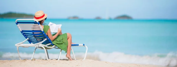 Joven mujer leyendo libro sobre chaise-lounge en la playa —  Fotos de Stock