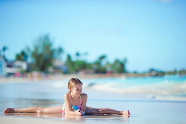 Adorable little girl lying in shallow water on white beach — Stock Photo, Image