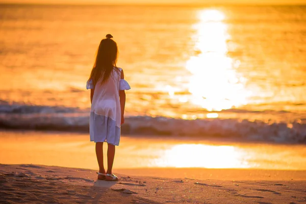 Urocza, szczęśliwa dziewczynka na białej plaży o zachodzie słońca. — Zdjęcie stockowe
