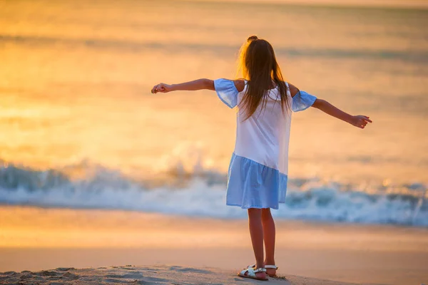 Urocza szczęśliwy dziewczynka, chodzenie po plaży o zachodzie słońca. — Zdjęcie stockowe
