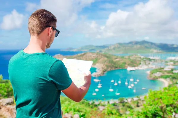 Young tourist man with map background of English Harbor from Shirley Heights, Antigua, paradise bay at tropical island in the Caribbean Sea — Stock Photo, Image