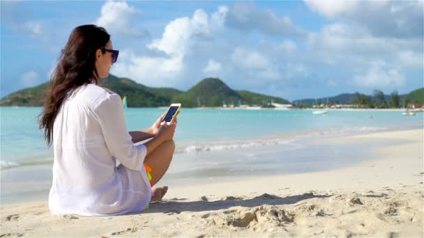 Jovem mulher com smartphone durante as férias na praia tropical. Menina bonita na praia com celular na ilha do Caribe. LOW MOTION — Vídeo de Stock