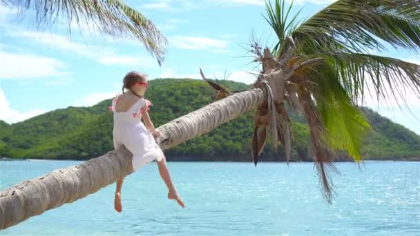 Kis lány ül a pálmafa és birtoklás sok móka trópusi tengerparton. A sziget Antigua Karib-tengeri nyaralás gyerek — Stock videók