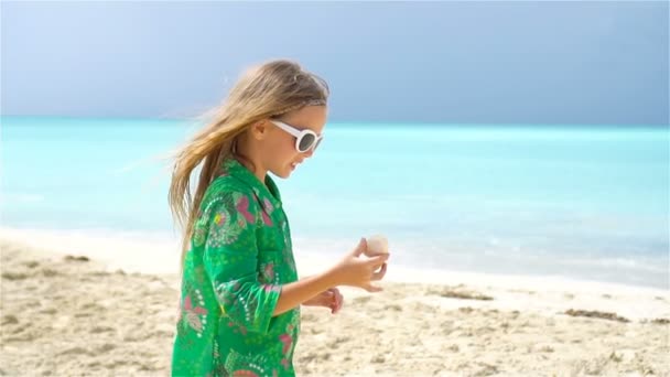 Schattig meisje met zeeschelp in handen op tropisch strand. Schattig meisje speelt met schelpen op het strand — Stockvideo