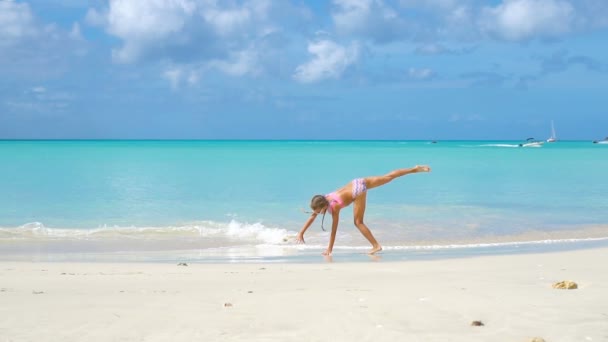 Aktives kleines Mädchen am Strand, das viel Spaß hat. Nettes Kind macht sportliche Übungen an der Küste — Stockvideo