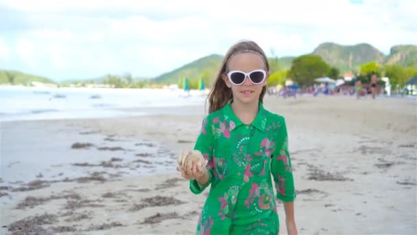 Kleines süßes Mädchen mit Muschel in den Händen am tropischen Strand. entzückendes kleines Mädchen spielt mit Muscheln am Strand — Stockvideo