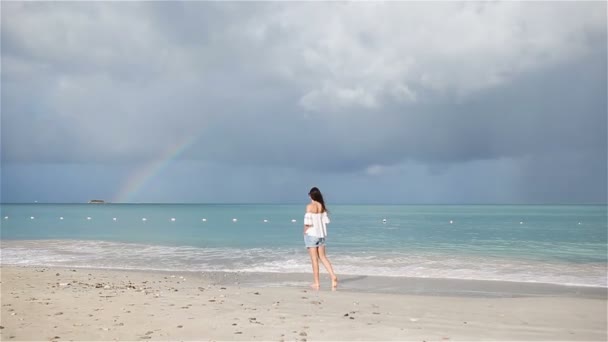 Young beautiful woman on tropical seashore with rainbow on background. Happy girl relaxing at white sand tropical beach — Stock Video