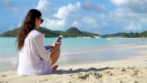 Mujer joven con teléfono en la playa tropical. Hermosa chica en la playa con teléfono celular en la isla caribeña — Vídeo de stock