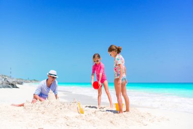 Tropikal beyaz Beach aile yapma Kumdan kale. Baba ve iki kız tropik sahilde kum ile oynamak