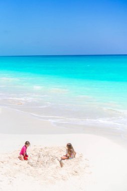 İki çocuk kumdan kale yapıyor ve tropikal sahilde eğleniyor.