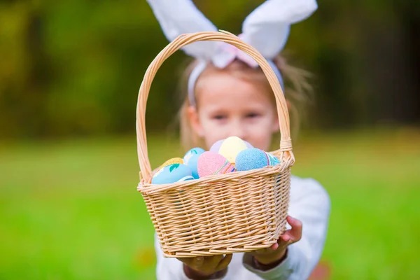 Adorable little girl wearing bunny ears with a basket full of Easter eggs on spring day outdoors — Stock Photo, Image