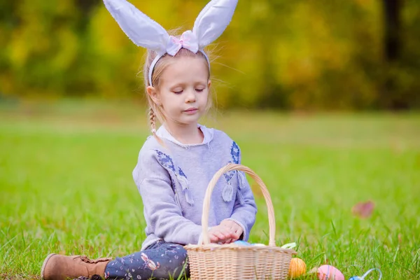 Adorable little girl wearing bunny ears with a basket full of Easter eggs on spring day outdoors — Stock Photo, Image