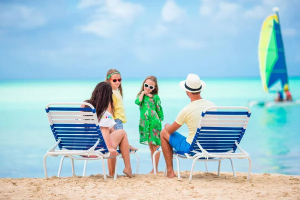 Feliz hermosa familia de cuatro en la playa. Los padres se relajan en la tumbona y los niños se divierten en la costa — Foto de Stock