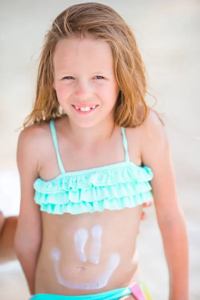 Kleines Mädchen amüsiert sich am tropischen Strand auf einer Liege mit Sonnencreme — Stockfoto