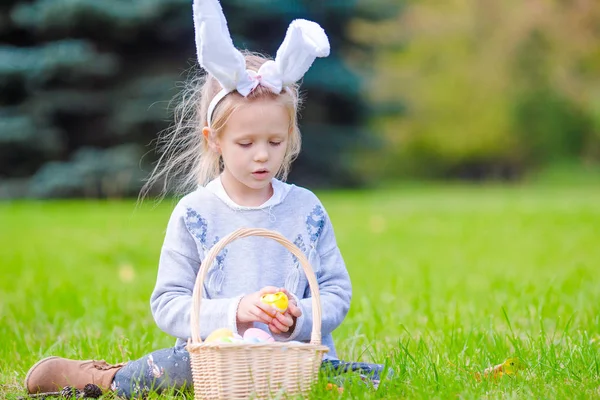 Portrait of little kid wearing bunny ears with a basket full of Easter eggs on spring day outdoors — Stock Photo, Image