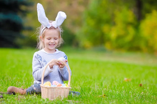 Portrait of little kid wearing bunny ears with a basket full of Easter eggs on spring day outdoors — Stock Photo, Image