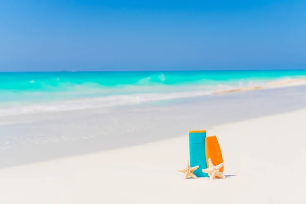 Botellas de crema solar, vasos, estrellas de mar en la playa de arena blanca — Foto de Stock