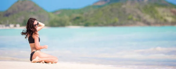 Frau sitzt lachend am Strand und genießt den Sommerurlaub und blickt in die Kamera. schönes Modell im Bikini im Sitzen. — Stockfoto