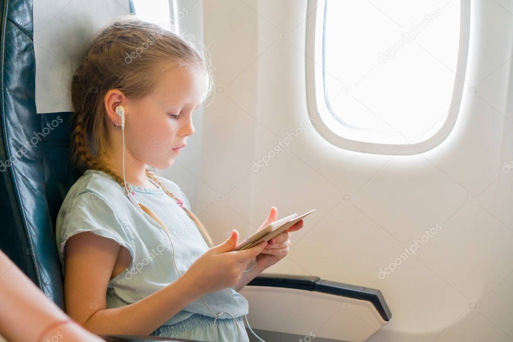 Adorable little girl traveling by an airplane. Cute kid with laptop near window in aircraft