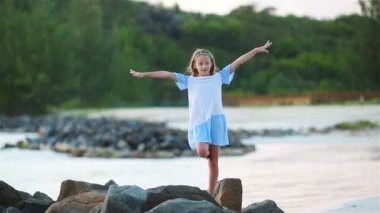 Gün batımında beyaz sahilde sevimli, mutlu küçük bir kız..