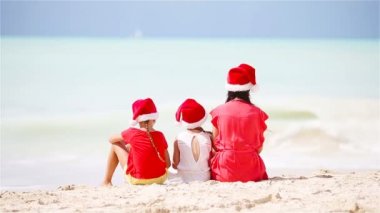 Noel Kutlamaları bir tropik sahilde kırmızı Santa şapkalar mutlu güzel aile. Anne ve çocuklar xmas tatil keyfini
