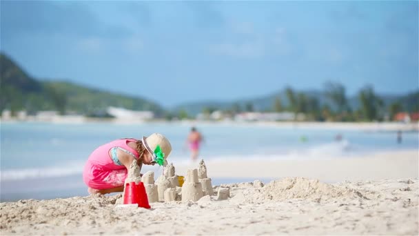 Entzückendes kleines Mädchen, das im Strandurlaub mit Spielzeug spielt. Kind bastelt eine Sandburg an der Küste — Stockvideo